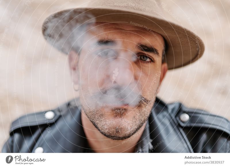 Serious pensive man in hat smoking cool smoke cigarette mustache hipster brutal rest contemplate male peaceful modern confident relax ponder concentrate