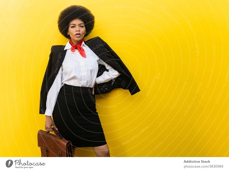 Stylish black woman in suit and blouse with briefcase style serious confident hand on waist executive respectable classy well dressed formal female studio shot