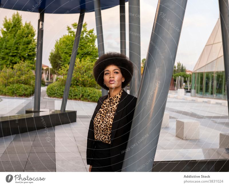 Pensive black woman leaning on metal post dreamy confident elegant think calm style peaceful serious formal female construction contemplate stand tranquil