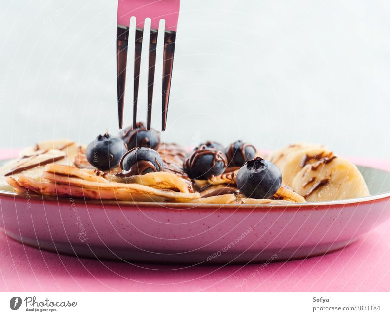 Eating crepes with chocolate and blueberries banana hazelnut fork chandeleur pink sweet breakfast closeup spread eat maslenitsa served pancake dessert