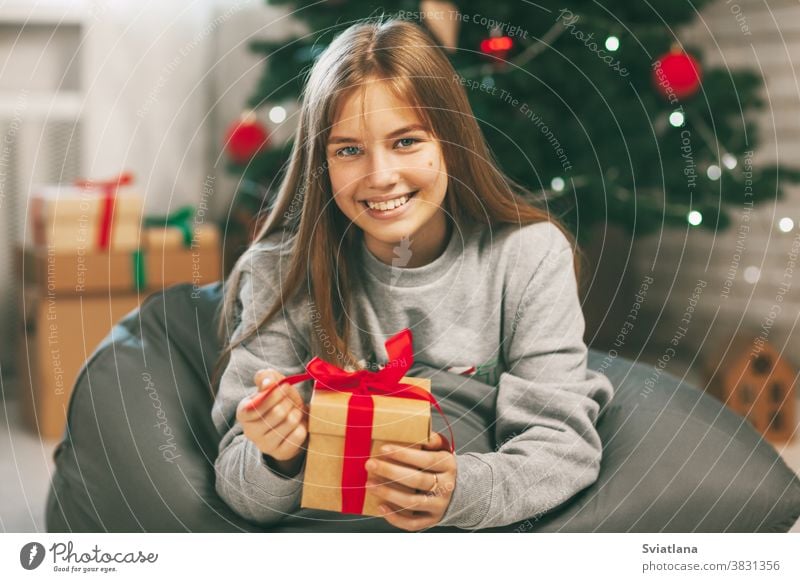 Beautiful teenage girl opens a gift made of kraft paper tied with a red ribbon, new year mood. Holiday concept of Christmas and New Year at home. christmas