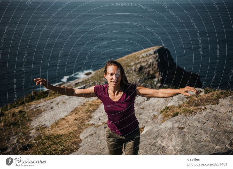 Woman raising arms while dance at the coastline on the top of a cliff, with sea in the background. nice inspirational sightseeing traveler elevation rock purple