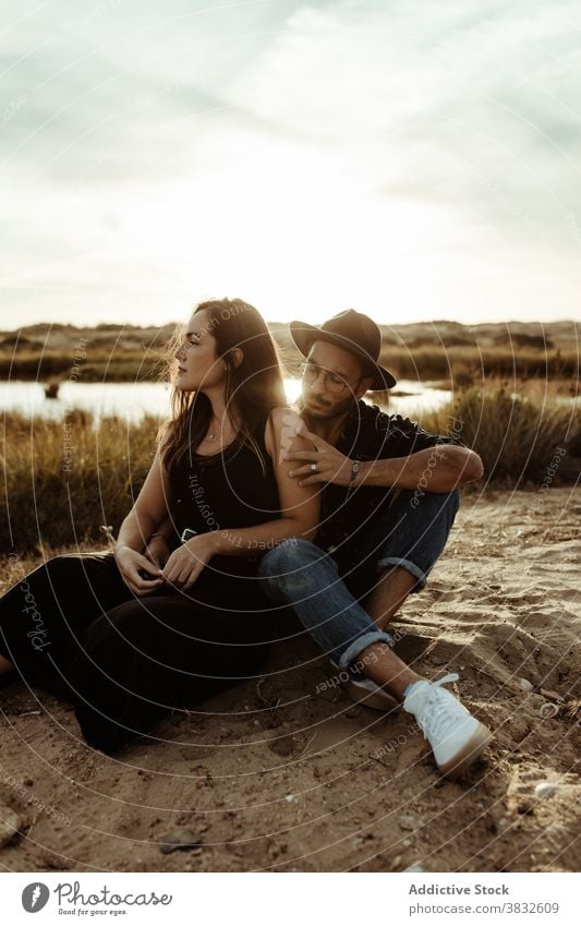 Dreamy couple on coast of pond at sunset love field affection relationship romantic meadow woman boyfriend girlfriend sit nature affair together hug embrace