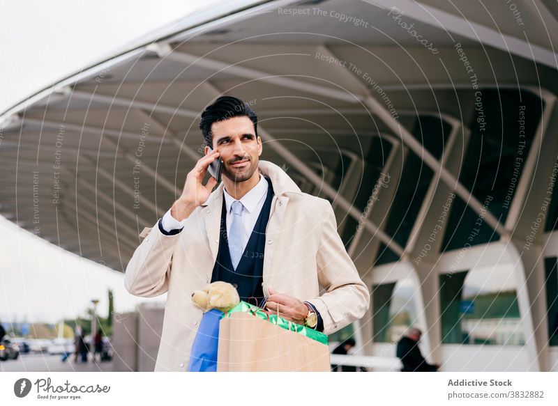 Man with shopper bags calling on phone near modern building man positive cheerful glad formal shopping bag businessman male ethnic black hair style speak