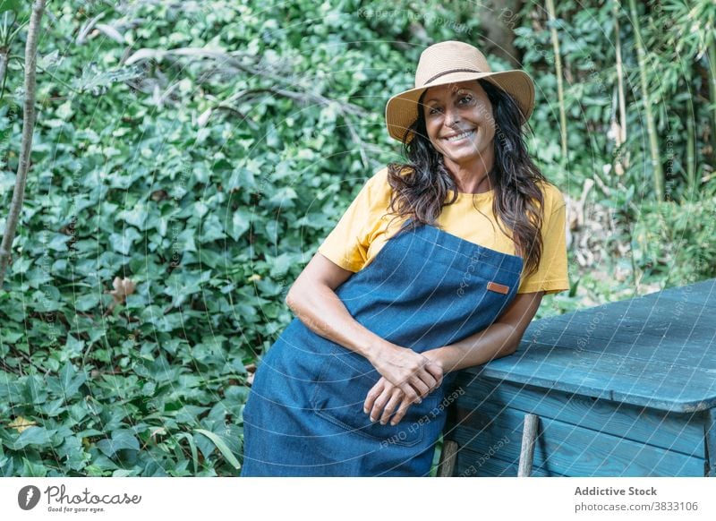 Cheerful woman with hat standing in green garden tropical happy positive foliage smile summer adult ethnic female lush plant nature cheerful lifestyle exotic