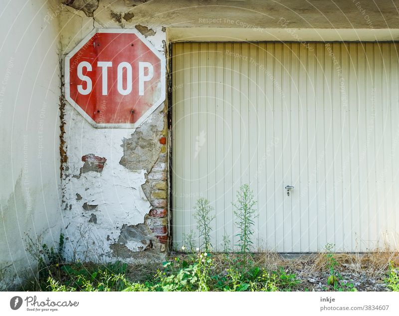 Stop sign next to garage door Colour photo Exterior shot Deserted Backyard Garage door street sign Red White Old Derelict Wall (barrier) Plaster Flaked off