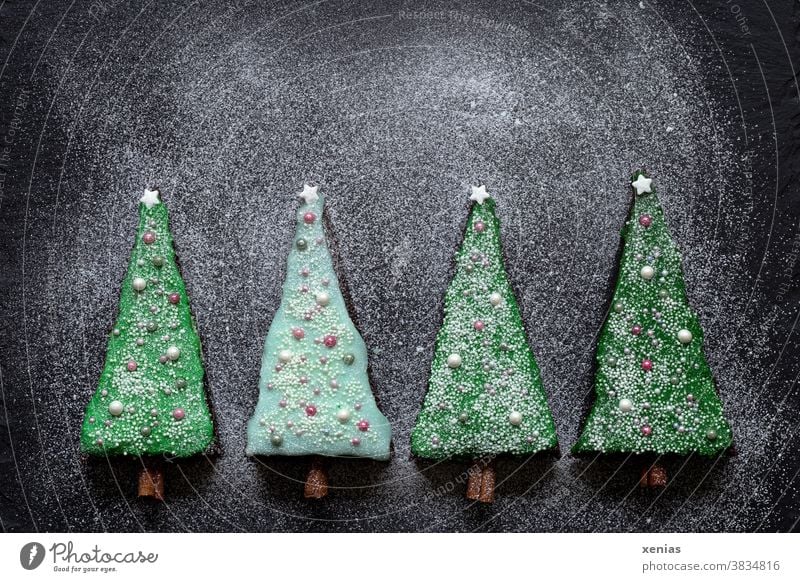 First one, then two, then three, then four pieces of cake as fir trees decorated with green icing lie on dark slate with icing sugar Cake Green Icing