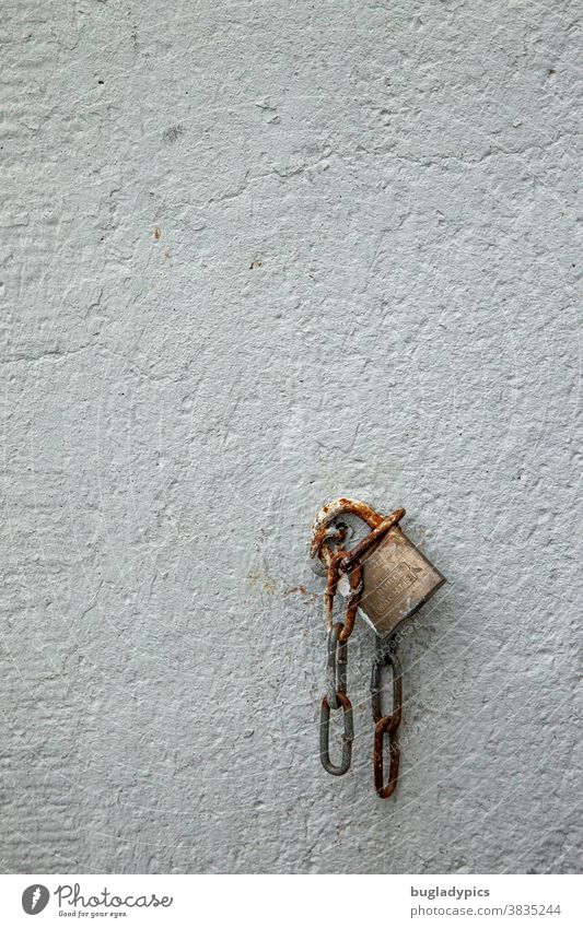 An old padlock/lock hangs together with a short chain on an eyelet on a white wall. Padlock Lock Chain Chain links Rust rusty Iron Metal Old Wall (building)