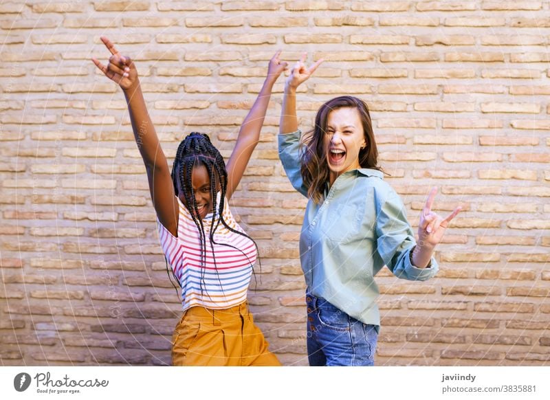 Two female friends having fun together on the street. Multiethnic friends. women multiethnic sign horn braids hairstyle black afro girl student two people