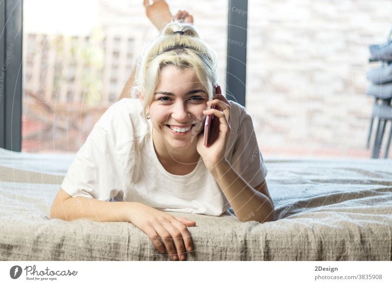 Close-up portrait of sweet attractive charming cute lovely adorable stunning cheerful blond lady lying on bed chatting boyfriend or husband in light white interior room indoors