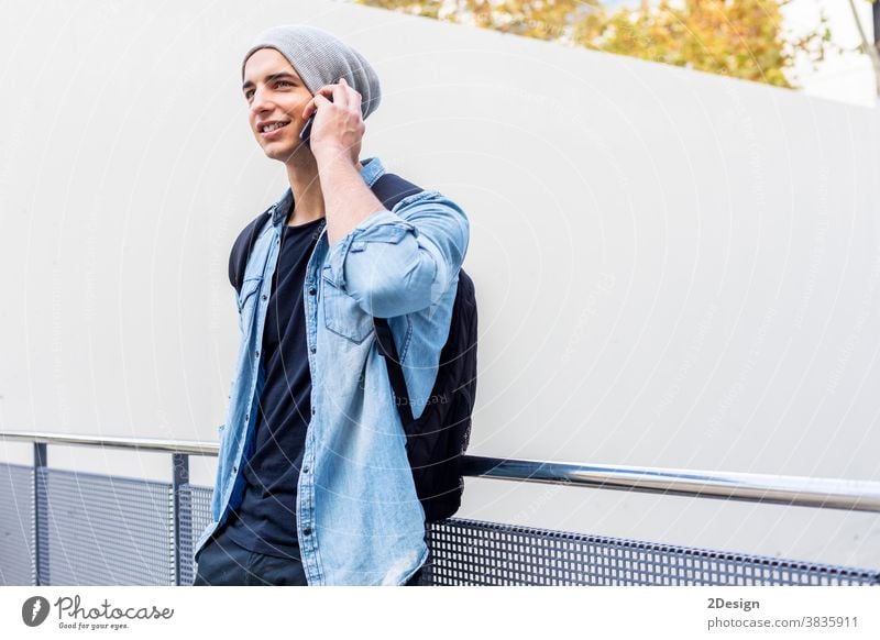 Urban stylish young man standing by the wall using cellphone smartphone talking calling guy mobile male technology city lifestyle urban communication