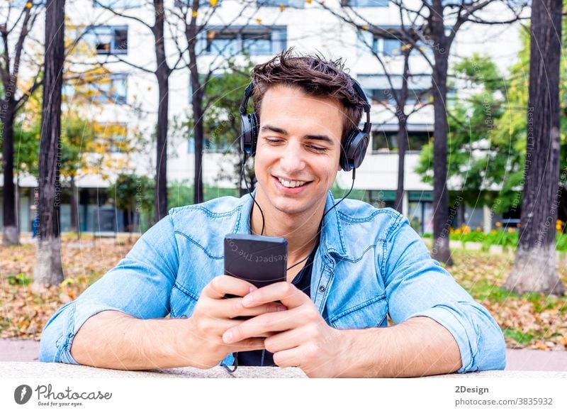 Young man looking at smartphone with headphone on his head headphones sitting earphones happy listening smiling young mobile guy technology person music