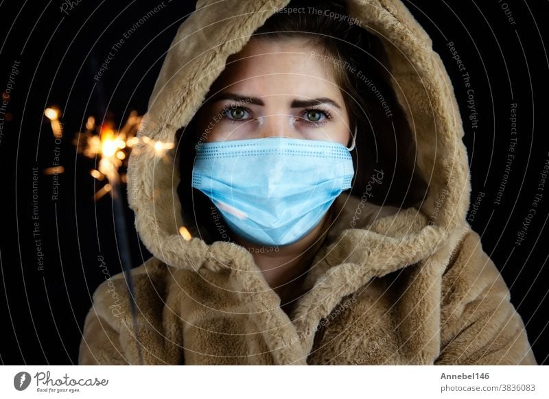 Happy new year, portrait of a young woman wearing medical mask and holding sparklers light in the dark for Covid-19, Coronavirus and New year concept