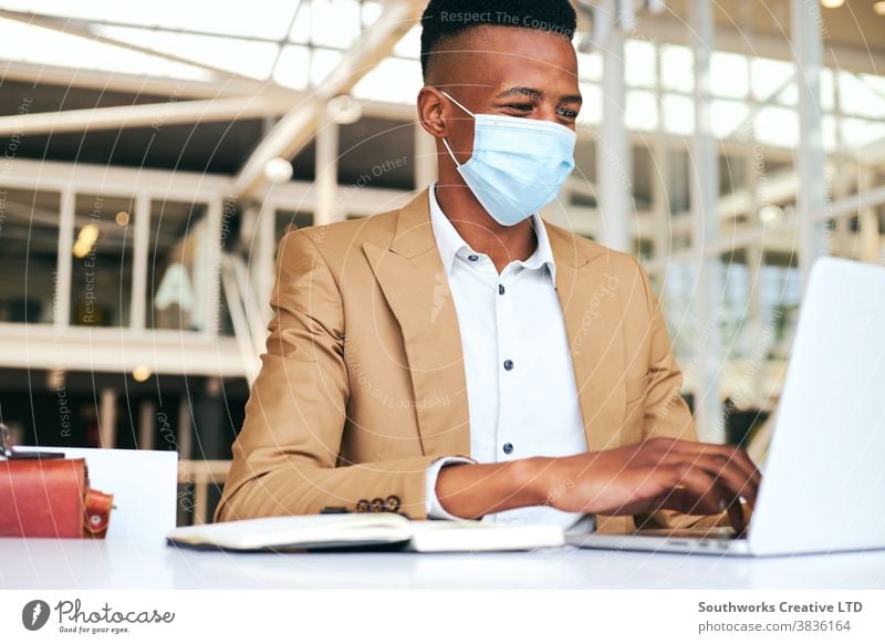 Young Businessman Wearing Mask Working On Laptop At Hot Desk In Office During Health Pandemic business businessman face mask face covering wearing ppe working