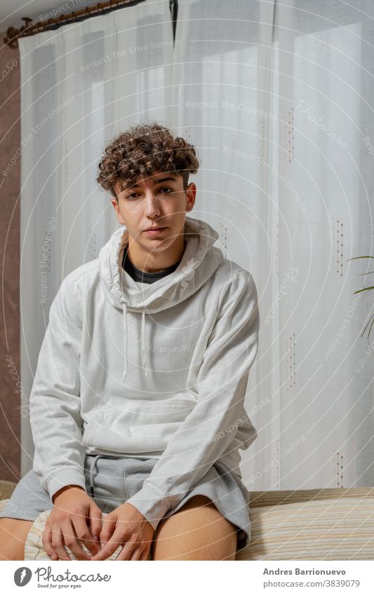 Attractive young man with curly hair wearing white sweatshirt posing on white curtains background cheerful casual smile male adult handsome happy attractive