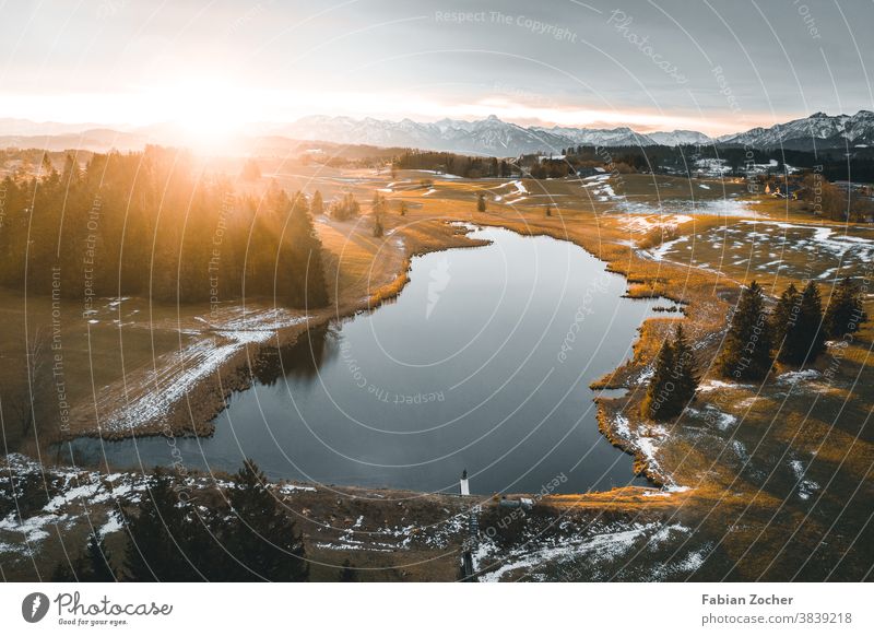 Sunrise over a mountain lake Allgäu Bavaria mountains Germany drone Europe Ground Pond Landscape Aerial photograph Nature Lake pond Water Sunbeam Spring Snow