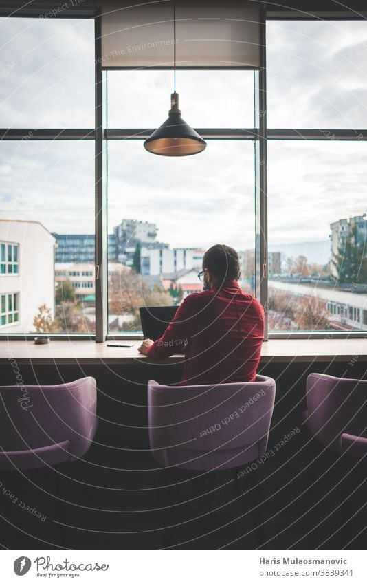 Modern man freelancer sitting in front of big windows and working on laptop turned back back view back view man business businessman coffee shop communication