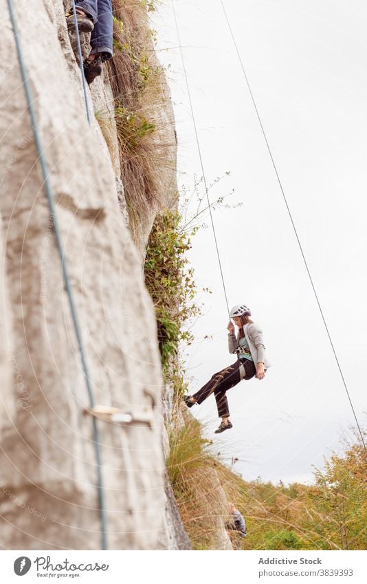 Strong female alpinist in safety equipment climbing on rocky cliff on sunny day woman mountaineer rope slope strong sportswear adventure extreme athlete climber