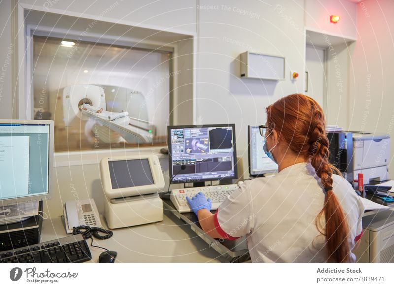 Unrecognizable radiologist working on computer during tomography diagnostic in clinic test monitor process equipment patient using gadget woman device ct