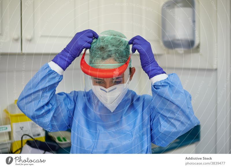 Anonymous medic in uniform putting on face shield in clinic put on medical sterile mask workplace professional woman protective doctor health care specialist