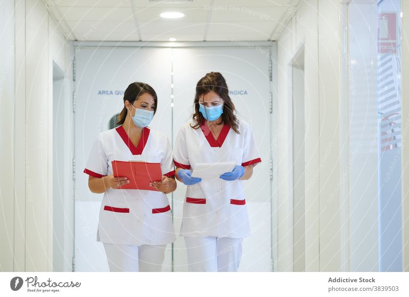 Anonymous nurses in uniforms with papers interacting in hospital passage medical staff profession walk women colleague folder colorful corridor professional