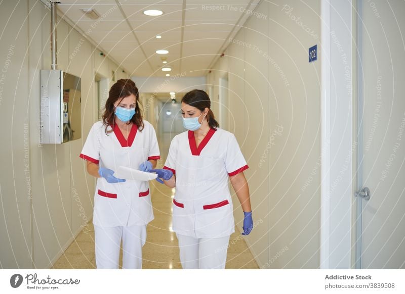 Anonymous nurses in uniforms with papers interacting in hospital passage medical staff profession walk women colleague folder colorful corridor professional