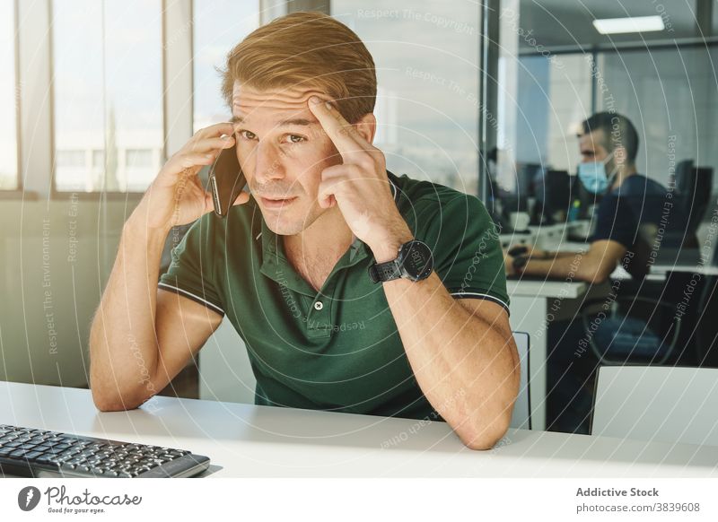 Male office worker talking on smartphone at table man discuss project smile workplace employee male cellphone busy business professional conversation modern sit