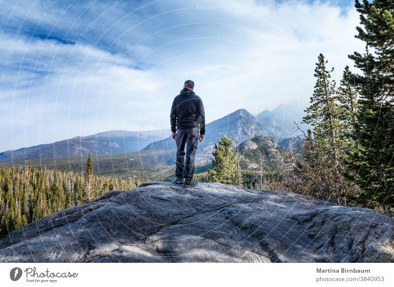 Man standing on a summit in the Rocky Mountain National Park and watching the smoke from the wildfires coming in the valley man tourist hiker caucasina