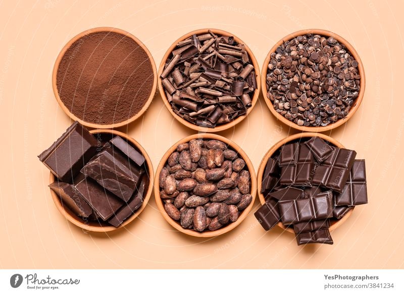 Chocolate pieces and cacao beans in bowls. Chocolate ingredient isolated on yellow background above view assortment baking beige bitter chocolate