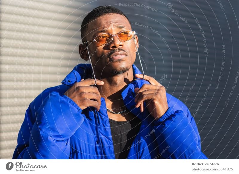 Stylish black man in sunglasses on street style orange trendy outfit determine cool urban male ethnic metal wall african american confident modern warm jacket