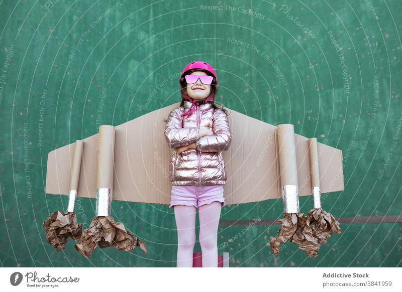 Smiling kid in cardboard jetpack looking up carton wing plane pilot child play achieve strength victory having fun celebrate success helmet cheerful girl