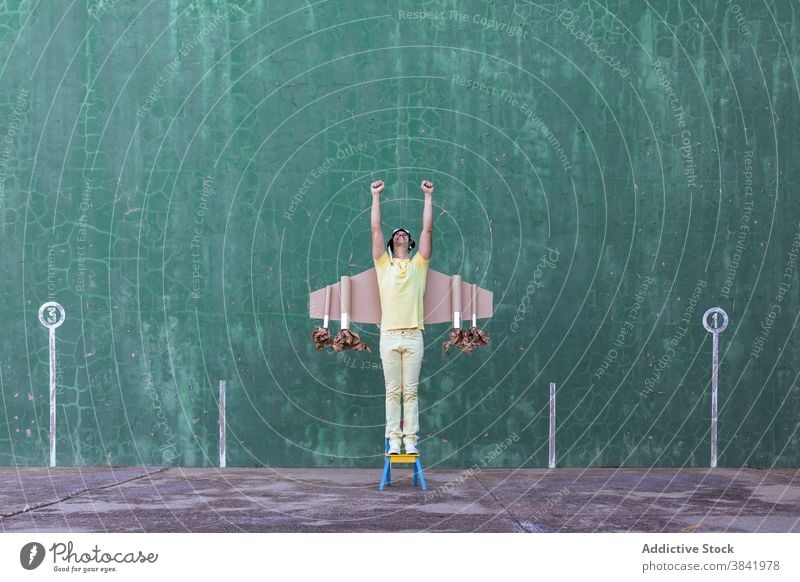 Energetic man with carton wings on street success victory achieve dreamy playful cheerful childish male handmade cardboard joy positive freedom optimist chair