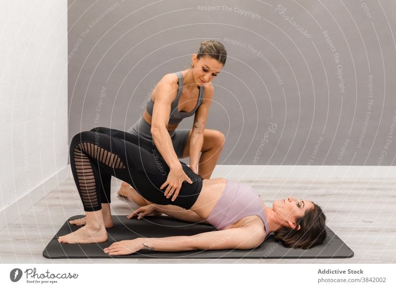 Slim woman doing yoga with trainer in studio class instructor women help support bridge pose flexible practice professional setu bandha sarvangasana fit harmony