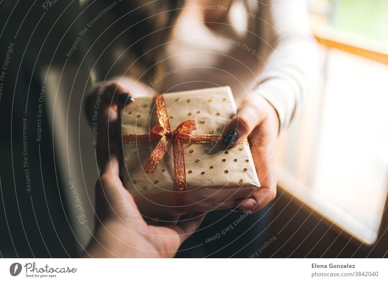 Young women with black glitter nails giving a Christmas present box to his friend. Hands hold new year gift box. decorated with craft paper, red and golden ribbon and stars. Family gift and holiday concept.