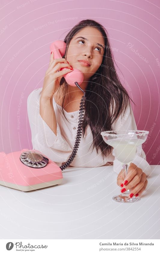 Cheerful and smiling young brunette woman with drink, uses a vintage phone. Portrait on a pink background beautiful brazilian disposable elegance fashion girl