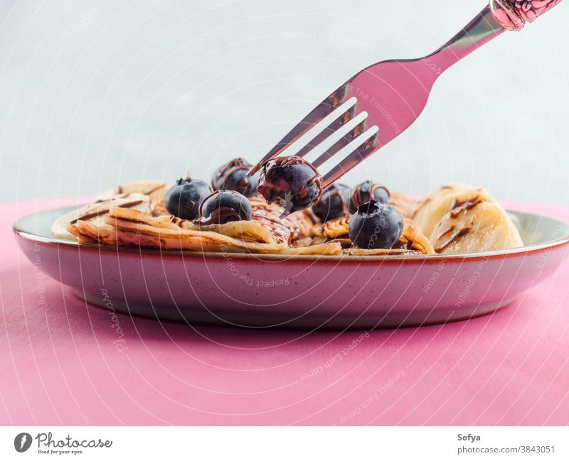 Eating crepes with chocolate and blueberries banana hazelnut fork chandeleur pink sweet breakfast closeup spread eat maslenitsa served pancake dessert