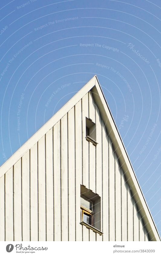 ingeniously designed house gable in white wood with two windows in front of a blue sky / optical illusion pediment house gables dwell