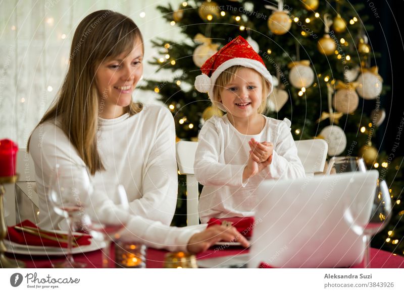 A happy family with a child is celebrating Christmas with their friends on video call using webcam. Family greeting their relatives on Christmas eve online. New normal  virtual event