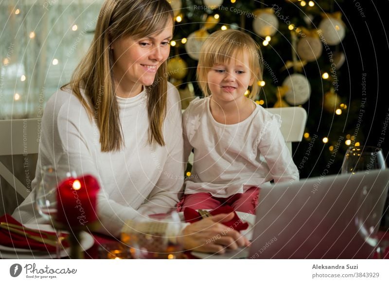 A happy family with a child is celebrating Christmas with their friends on video call using webcam. Family greeting their relatives on Christmas eve online. New normal  virtual event