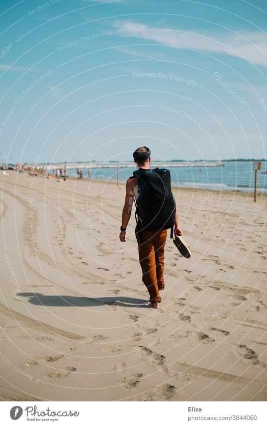 A man with a backpack walks along a beach on vacation and looks at the sea. Beach Man Backpack stroll travel voyager Sandy beach Vacation & Travel Human being