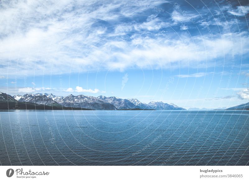 A fjord in Norway. In the foreground the sea and in the background snow-covered mountain tops. The blue sky is decorated by veil clouds. Fjord Ocean coast