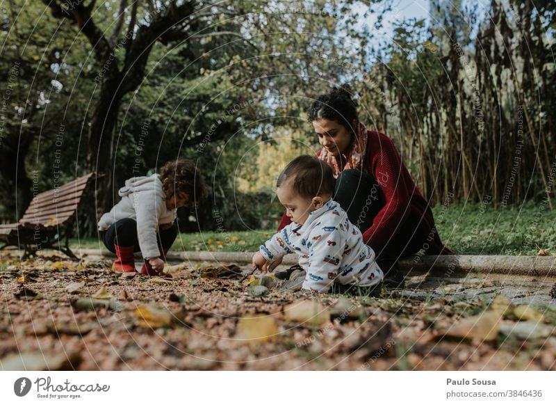 Mother playing with two children outdoors 0-09 years 30-39 years affectionate authentic autumn caring casual caucasian color curiosity curly hair daughter day