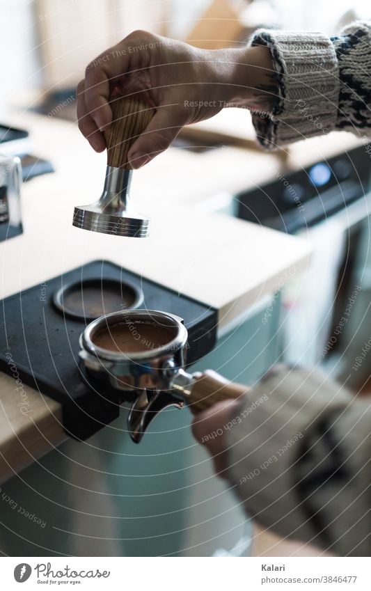 Barista with wool jacket presses the espresso powder into the portafilter with a tamper barista Espresso Coffee Café screen carrier Woman prepare Close-up Hand