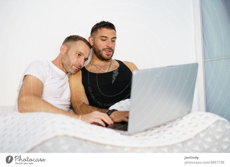 Gay couple consulting something on their laptop while lying on the bed. gay men homosexual lgbt lgbtq male relationship boyfriend people 30s togetherness man