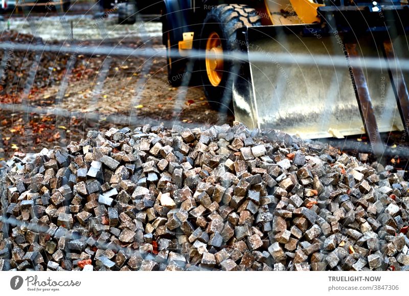 Road construction and landscaping with a heavy yellow wheel loader, thick black tyres and a large loading shovel in front of a pile of small cobblestones