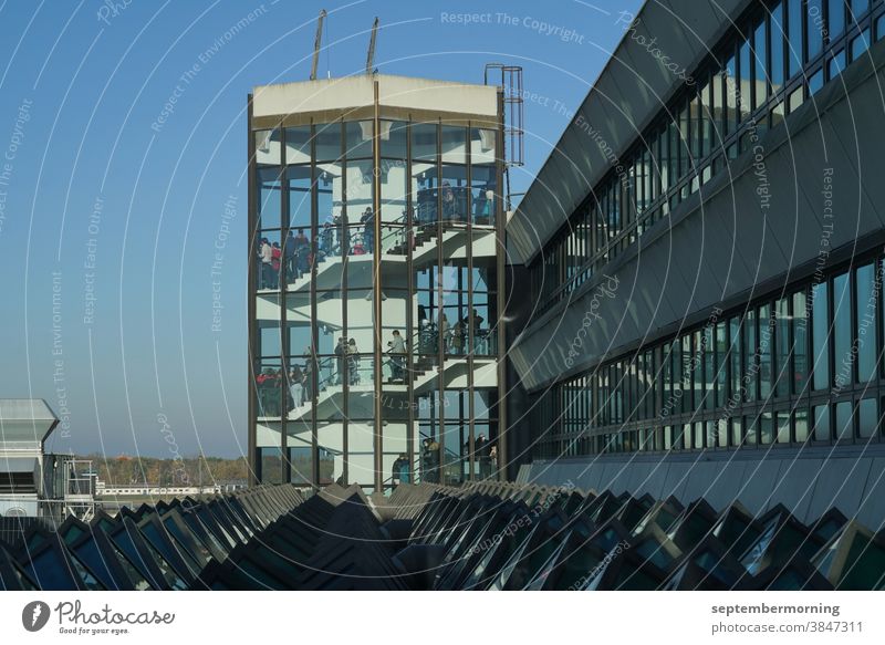 Tower made of glass, internal stairs, many people on the steps, light blue sky, building complex connects to the tower, steel construction Tower transparent