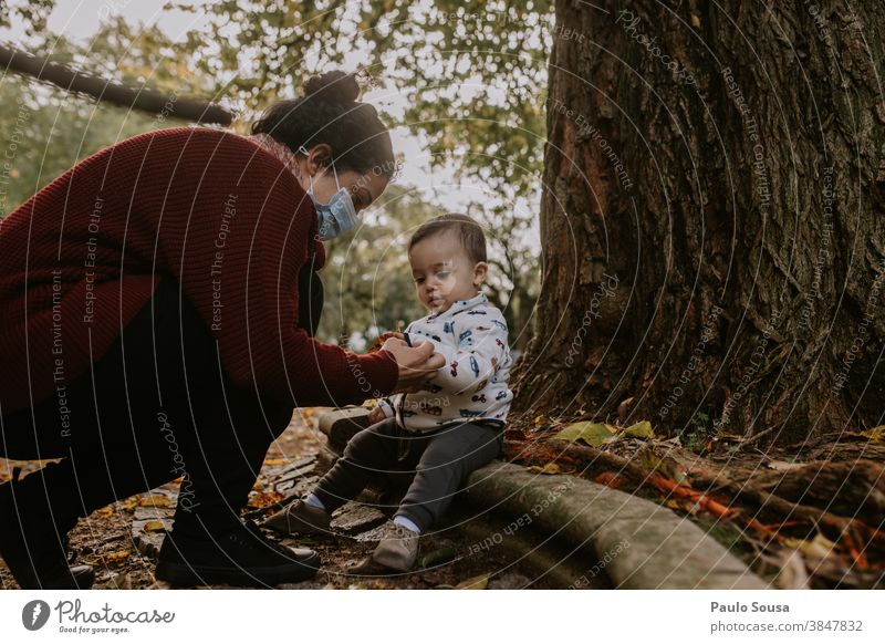 Mother with mask and toddler at the park 0-09 years 30-39 years affectionate authentic autumn caring casual caucasian child color curly hair day enjoyment