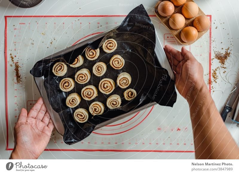 Man's hand holding a tray of cinnamon rolls ready to be put in the oven. indoor cooking dough flour chef restaurant employment food Eggs bakery desserts butter