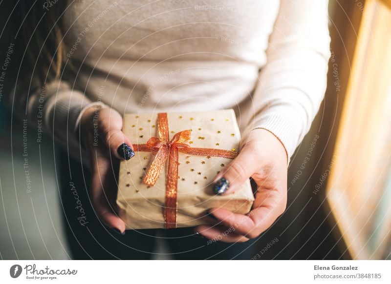 Young women with glitter nails holding Christmas present box and showing it in camera. Hands hold new year gift box. decorated with craft paper, red and golden ribbon and stars. Family gift concept.