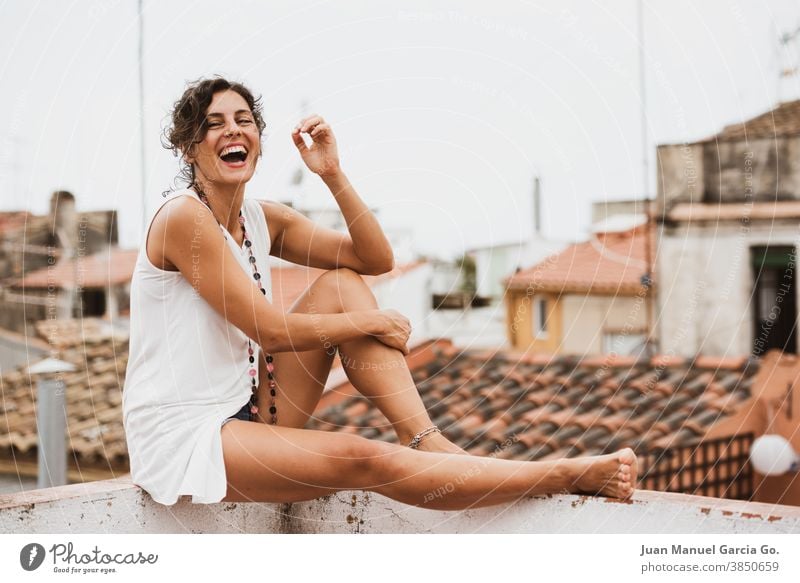 Young woman in white blouse laughs out loud laughter barefoot shoeless tanned rural overcast fit edge dress tiles pendant roof shirt cloudy necklace curly